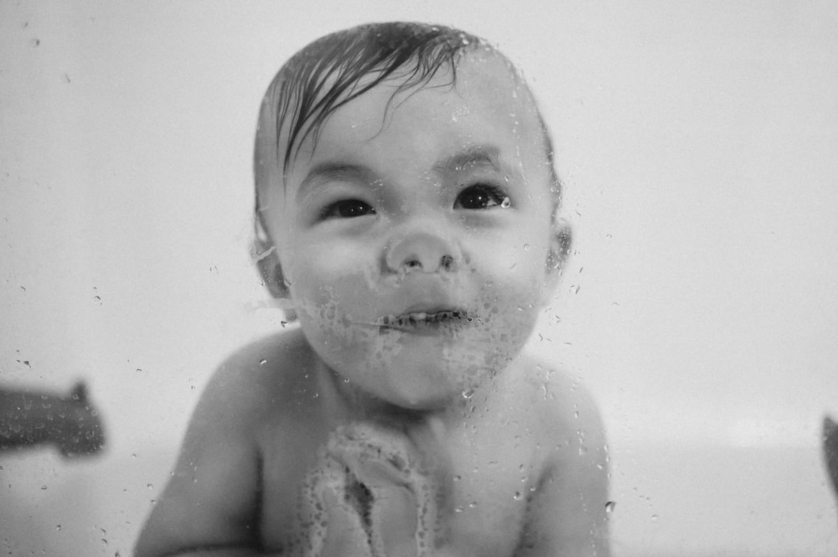 Black and white lifestyle photo of a little boy being silly, pressing his nose up against glass.