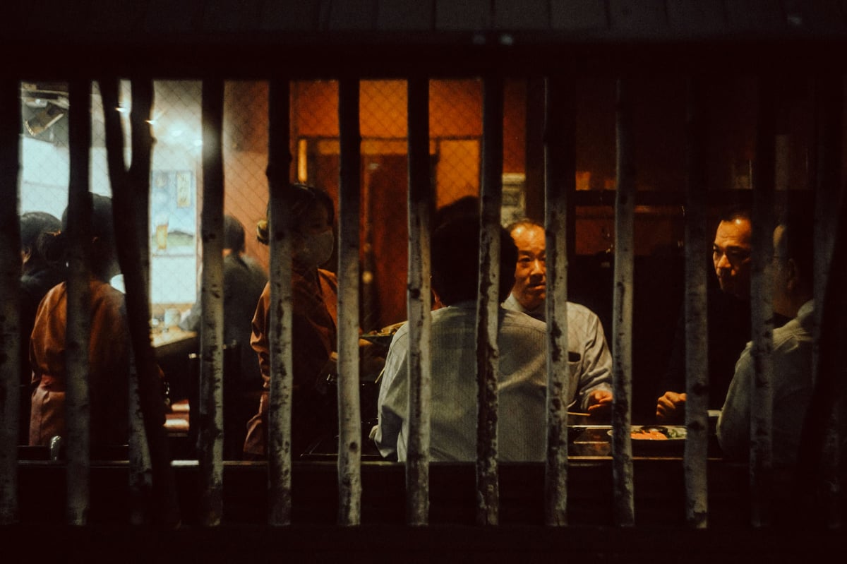 Japanese men eating inside a restaurant. Photo taken from outside the restaurant.