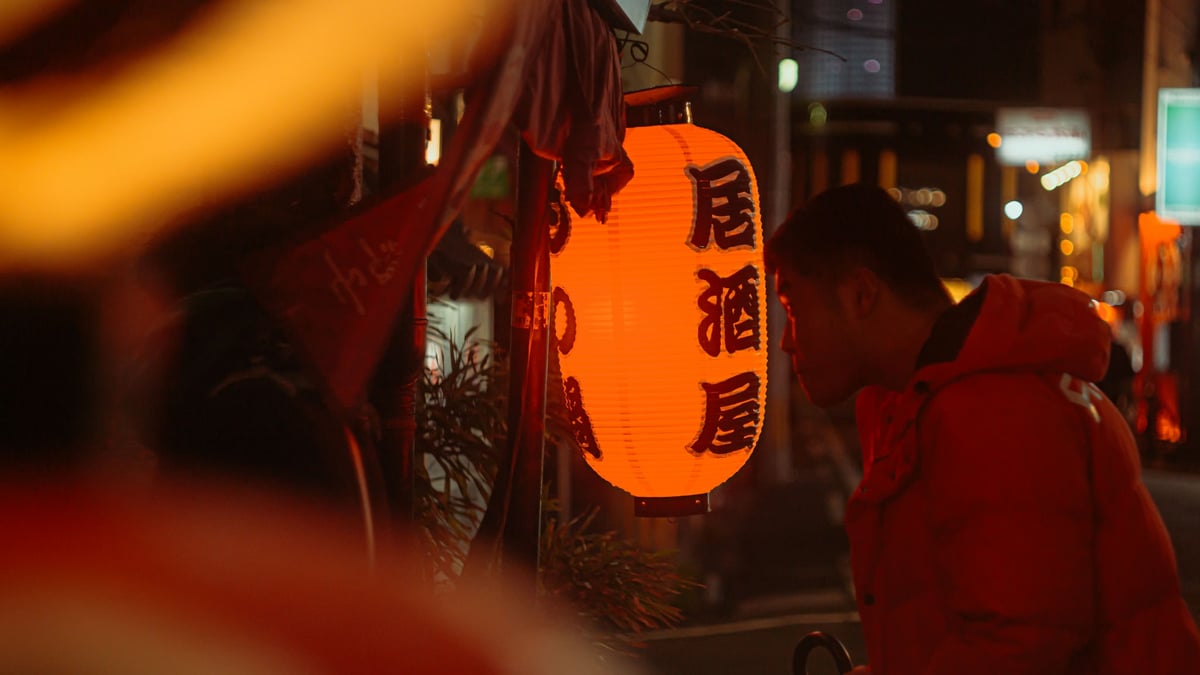 A man checks the menu of a restaurant lit only by an orange Japanese lantern.